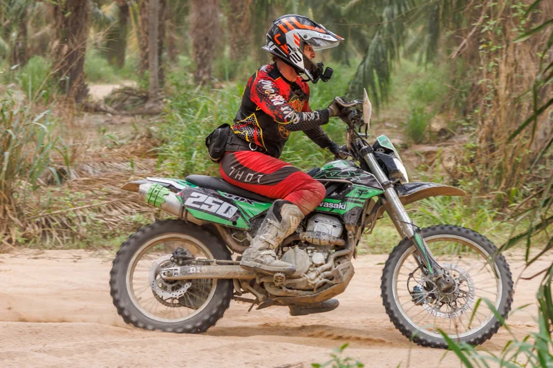 Rider on a green dirt bike moving across the trail
