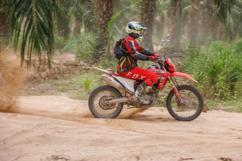 Rider on a red dirt bike crossing an open sandy trail